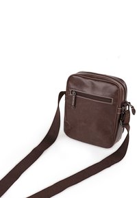 Bolso cruzado de cuero marrón con forma rectangular, un bolsillo frontal con cremallera y una correa de tela larga y ajustable. Textura suave, con un diseño minimalista.