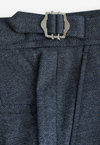 Dark blue trousers with a textured fabric, featuring a prominent metallic belt buckle and pleated design.
