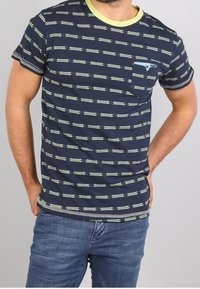 T-paita tummansinisestä puuvillasta, jossa on vaaleanvihreitä vaakaraitoja, ribattu pyöreä kaula-aukko, lyhyet hihat ja tasku, jossa on sininen yksityiskohta.