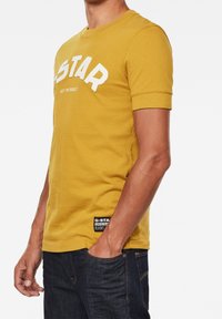 Mosterdgele t-shirt met korte mouwen, voorzien van een witte "G-STAR" logo en de tekst "JUST THE PRODUCT", met een gestructureerde katoenen stof, zwart label aan de zoom.