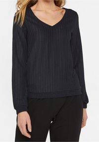 Svart ribbad långärmad tröja med V-ringning och elastisk fåll. Har ett texturerat tyg och åtsittande ärmar. Lämplig för vardagsbruk.