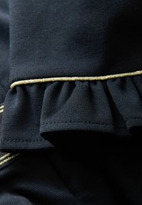 Un tissu noir à la texture lisse présente un ourlet froncé au premier plan, accentué par une bordure dorée le long du bord.