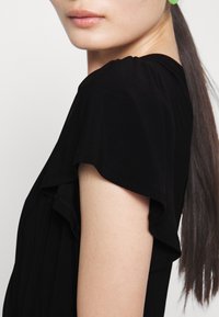 Svart klänning med fladdrande ärmar, mjuk textur, åtsittande kjol och flödande nederdel. Närbild på axeln och armen. Inga synliga mönster eller detaljer.