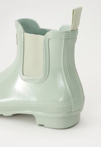 Botte en caoutchouc vert menthe à la cheville avec panneau latéral élastique, semelle texturée et tirette à l'arrière. Fini lisse avec des détails subtils.