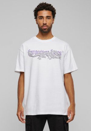 Hvid T-shirt i bomuld med et lilla dragegrafik på forsiden, i en afslappet pasform med rund halsudskæring. Sorte bukser synlige nedenunder.