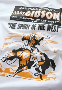 Cowboy lovagol egy herélő ló hátán lasszóval, a szöveg így szól: Hoot Gibson, "A Nyugat Bajnoka" a "Nyugat Lelkében."
