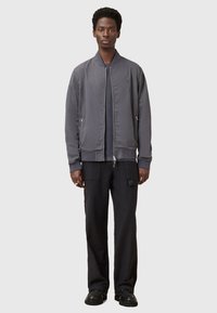 Giacca bomber grigia con zip frontale, polsini a coste e due tasche laterali, abbinata a pantaloni cargo neri e scarpe nere. Texture liscia e opaca.