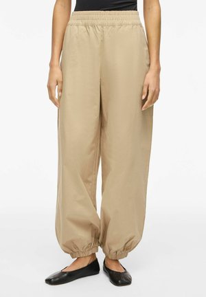 Bézs színű, bőszárú nadrág, elasztikus derékrésszel és összehúzott elasztikus szegélyekkel, fekete balerinával és fekete felsővel viselve.