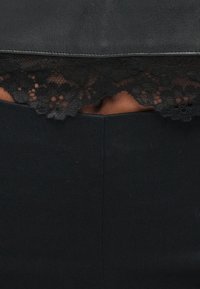 Top crop din piele neagră cu tiv din dantelă în partea de jos. Dantela are un model floral complex, creând un efect de textură contrastantă.