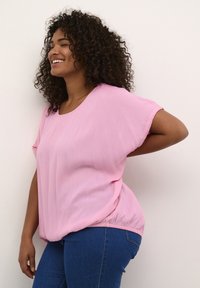 Lyserød kortærmet top med rund halsudskæring og let gathered kant, parret med mørkeblå tætsiddende jeans. Glat tekstur, afslappet pasform.
