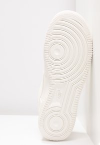 Suola di sneaker bianca con motivi circolari e ondulati, bordi testurizzati e caratteristiche arrotondate. Il materiale sembra gomma con una finitura liscia.