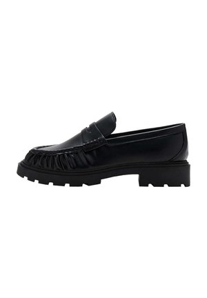 Mocasín negro de cuero con suela gruesa, detalles de costuras y una tira tipo "penny" en la parte superior.