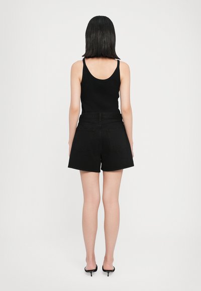 Shorts en denim noir à taille haute, dotés de poches arrière et d'une coupe décontractée. Portés avec un débardeur noir et des talons fins noirs.