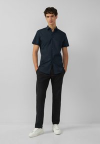 Kurzarm Hemd in Marineblau mit Knopfleiste, taillierte Passform und glatter Textur, kombiniert mit schwarzen Hosen und weißen Sneakers.