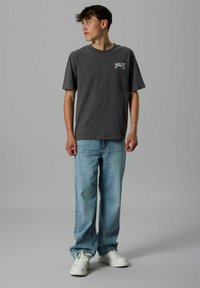 Grå t-shirt med korte ærmer og brystlomme, parret med lyseblå afslappede jeans og hvide sneakers.