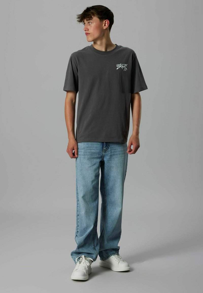 Grå t-shirt med korte ærmer og brystlomme, parret med lyseblå afslappede jeans og hvide sneakers.