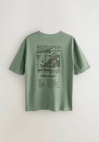Grünes Baumwoll-T-Shirt mit kurzen Ärmeln, das ein Retro-Design mit Text und Grafiken im Zusammenhang mit einem Pink Floyd Konzert zeigt.