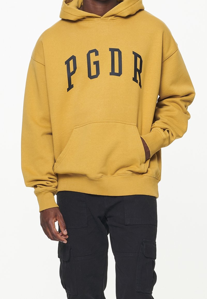 Gelber Hoodie mit schwarzer "PGDR"-Beschriftung auf der Brust. Hergestellt aus weichem Stoff, mit Kängurutasche und gerippten Bündchen.