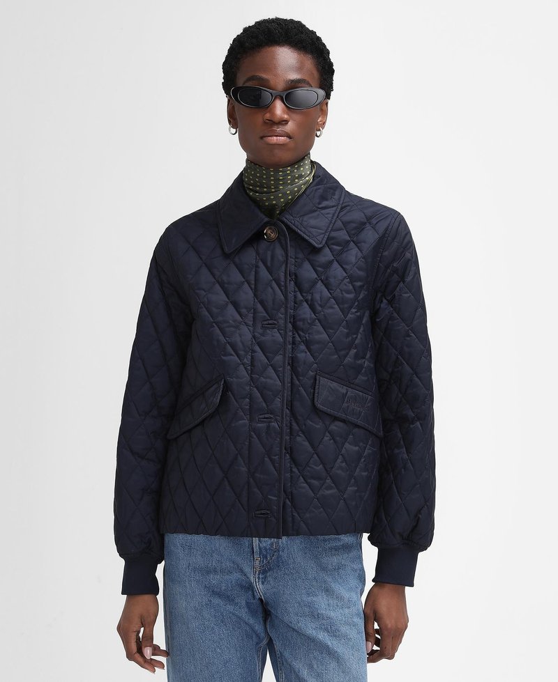 Navy quilted jacket with button closure and two front pockets. Features a collar and ribbed cuffs, paired with a polka dot scarf.