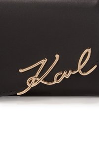 Czarny skórzany portfel z wyraźnym złotym detalem z podpisem "Karl" na przedniej stronie, podkreślający gładką fakturę i elegancki design.