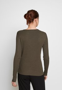 Dopasowany prążkowany top z długim rękawem w ciemnooliwkowym kolorze, z okrągłym dekoltem. Wykonany z miękkiej, teksturowanej tkaniny.