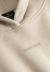 Hanorac bej dintr-un material moale, cu buzunar tip kangaroo în față. Prezintă un logo texturat "JOHNNY URBAN" brodat în zona pieptului.