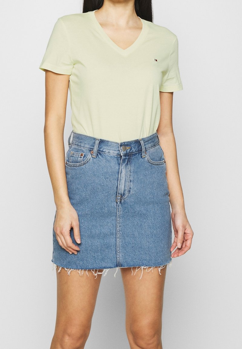 Helles Gelb, kurzärmliges V-Ausschnitt-T-Shirt, kombiniert mit einem taillierten blauen Jeans-Minirock mit fransigem Saum und klassischem fünf-Taschen-Design.