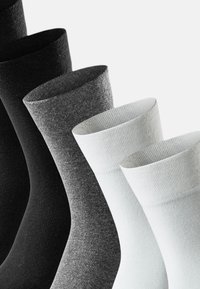 Calzini neri, grigio scuro, grigio chiaro e bianchi disposti in un gradiente. Presentano una parte superiore a coste e una texture liscia.
