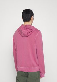 Różowa bluza z luźnym krojem, z kapturem na sznurku, ściągaczami w mankietach i u dołu. Gładka tekstura z farbowanym wykończeniem.