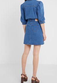 Denimový dvoudílný outfit skládající se z kráceného topu s nabíranými rukávy a sukně ke kolenům. Modrá barva, sukně má zadní kapsy.