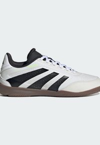 Witte en zwarte lage sport schoenen met drie zwarte strepen en een bruine zool, voorzien van witte veters en een zwarte gewatteerde kraag.