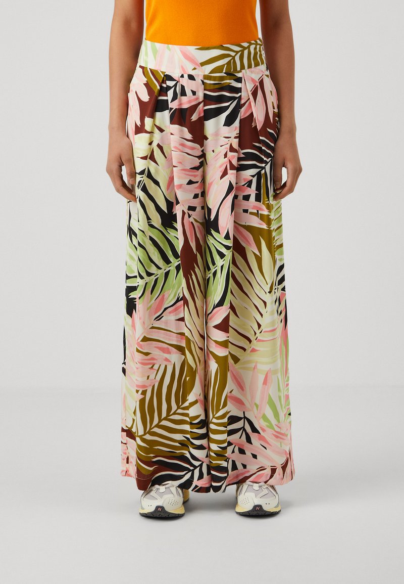 Falda maxi con un estampado de hojas tropicales en verde, rosa y marrón. Fabricada con un tejido ligero y con plisados, combinada con zapatillas deportivas.