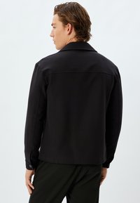 Giacca nera con un design colletto, maniche lunghe e polsini abbottonati. Texture liscia, vestibilità su misura e stile minimalista.