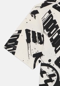 Grafisk t-skjorte med kremfarget bakgrunn, med fet svart tekst og sprute-design, korte ermer og laget av bomull.