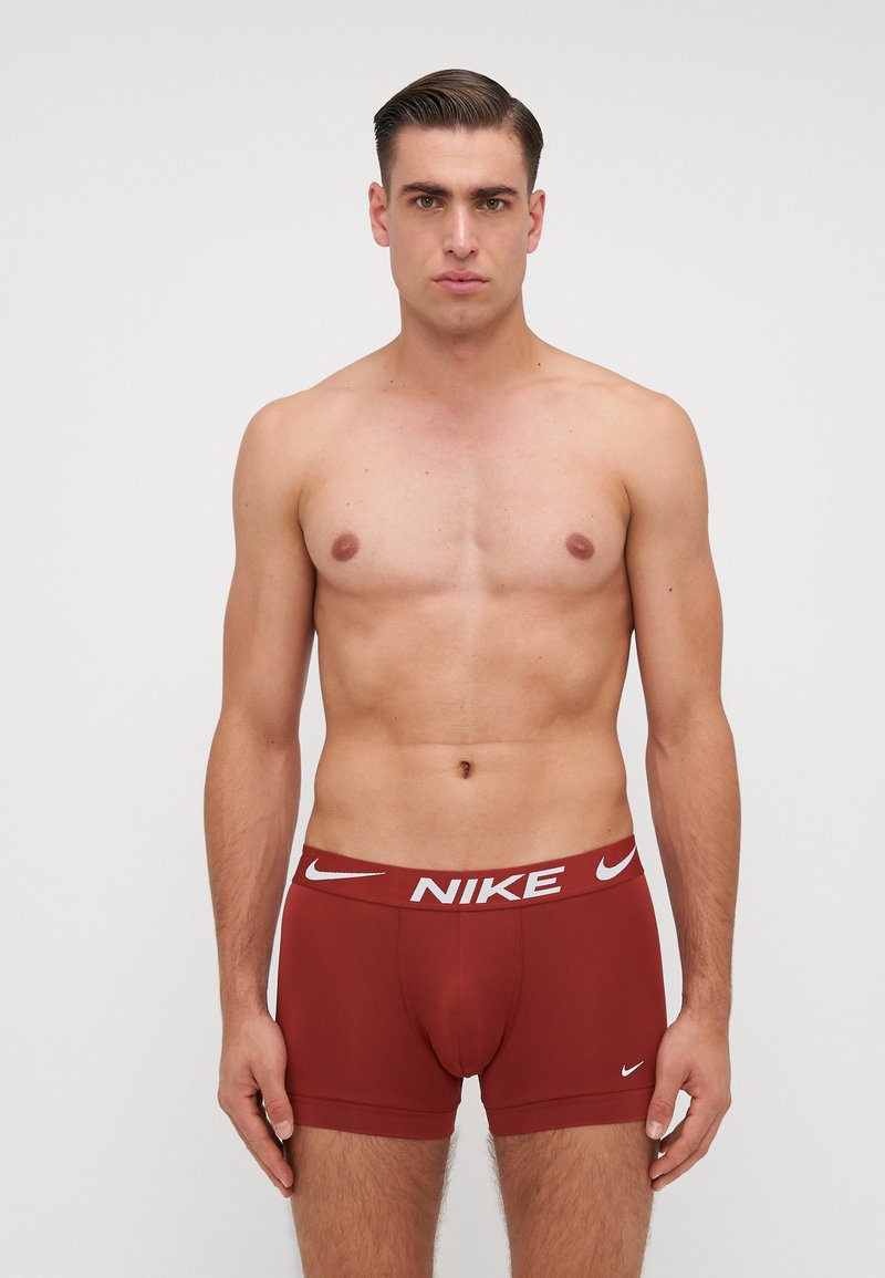 Boxeri Nike roșii din țesătură netedă și elastică, cu un brâu alb cu logo. Au un design ajustat, subliniind forma și susținerea.