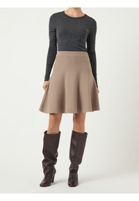 Jupe évasée marron en tissu texturé, associée à un haut gris à manches longues et des bottes en cuir marron montant jusqu'aux genoux.