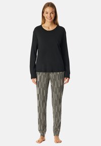 Zwarte langemouwen top gecombineerd met zwart-witte gestreepte pyjamabroek. Zacht materiaal, relaxte pasvorm en elastische manchetten bij de broek.