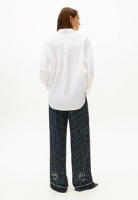 Camisa blanca de botones con un diseño de espalda partida, combinada con pantalones navy de patrón que presentan diseños circulares y acentos de paisley.