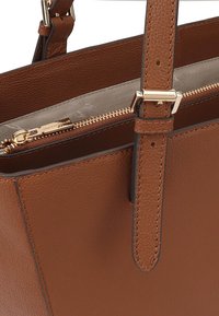 Bruine leren handtas met een gestructureerd oppervlak, gouden ritsbeslag en een afneembare schouderriem. De binnenkant heeft een lichte stofvoering.