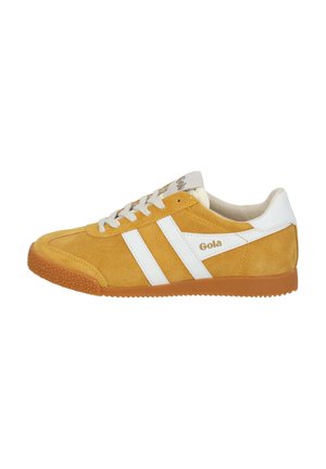 Zapatilla de ante amarilla con rayas blancas, suela de goma texturizada y cordones color crema. Logo presente en el lado y en la lengua.