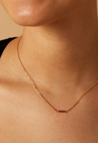 Gouden ketting met een delicaat barpendant waarop vijf rode edelstenen zijn geplaatst, met een gladde textuur en eenvoudig ontwerp.
