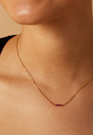 Gouden ketting met een delicaat barpendant waarop vijf rode edelstenen zijn geplaatst, met een gladde textuur en eenvoudig ontwerp.