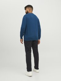 Blå långärmad tröja med rund halsringning, texturerad tyg och ribbade mudd, som matchas med svarta byxor och vita sneakers.
