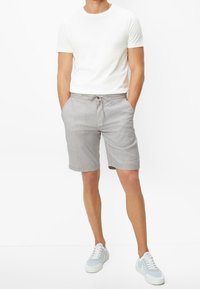 Hellgraue Shorts mit strukturiertem Finish, ausgestattet mit einem verstellbaren Kordelzugbund. Kombiniert mit einem taillierten weißen T-Shirt und hellen Sneakers.