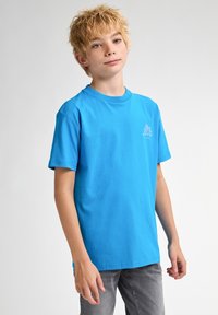 Camiseta azul de algodón de manga corta y cuello redondo. Presenta un pequeño diseño de logo azul claro en el pecho. Corte recto, textura suave.