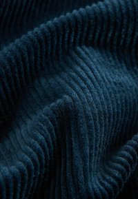 Tessuto in corduroy testurizzato di un profondo blu navy, caratterizzato da evidenti righe verticali e una sensazione morbida e vellutata, che mette in mostra fibre fini.
