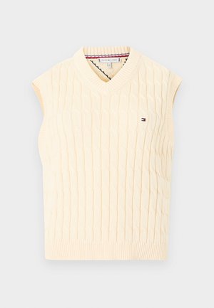 Kabelstrikket ermeløs genser i kremfarge, med dyp V-hals og ribbet kant. Lite logo på brystet. Jevn tekstur med strukturert design.