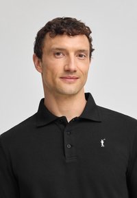 Zwarte polo met een textuurstof, voorzien van een kraag, een knoopsluiting met drie knopen en een klein wit golferlogo op de linkerborst.