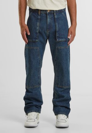 Blue denim cargo pants with multiple pockets, loose fit, and zippered cuffs, featuring contrast stitching and a button closure at the waist.