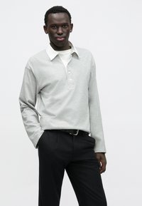 Helehall pika varrukaga polomees, valge krae ja nööpidega esiosa, mustade lõigatud pükstega. Sile kangast tekstuur.